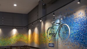A waiting area with a bicycle mounted on the wall, a leather chair, and a table with chairs. - Monreale Express Ribeirão Preto (Ribeirão Preto)