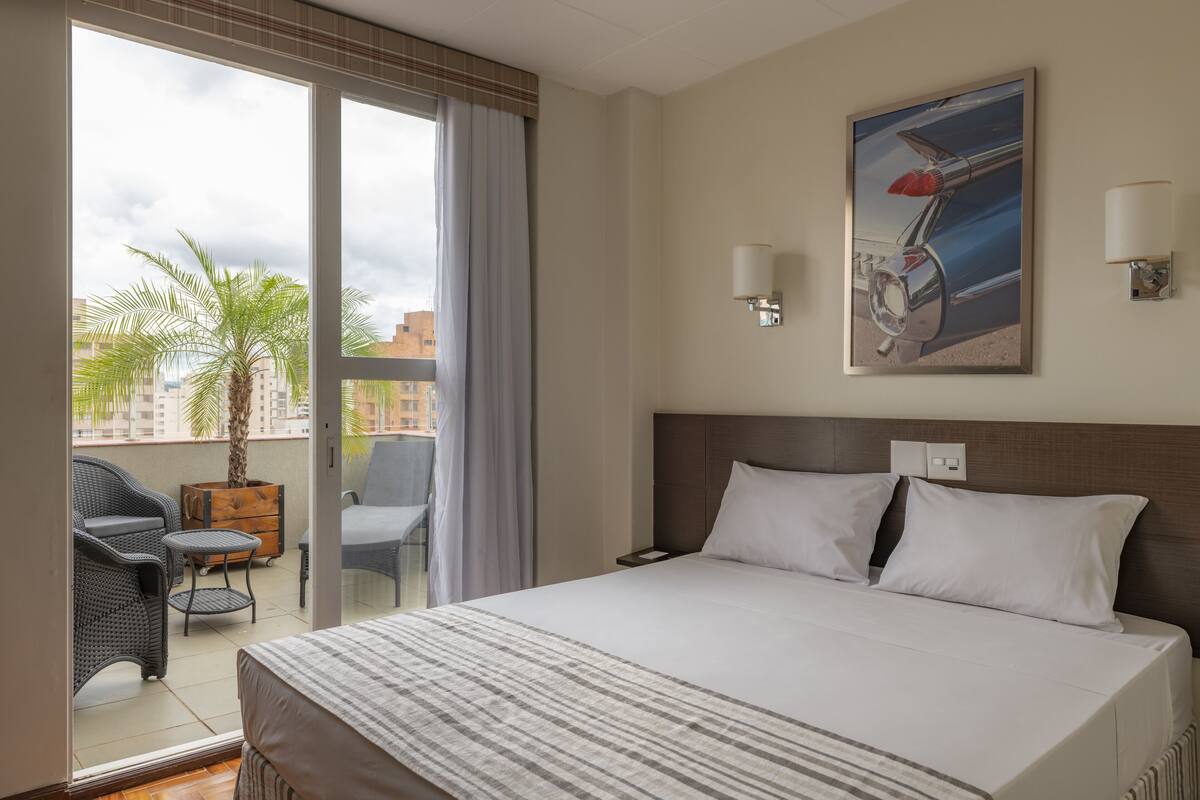 Ein Hotelzimmer mit einem großen Bett, einem Balkon mit einer Palme und Blick auf die Stadt.
