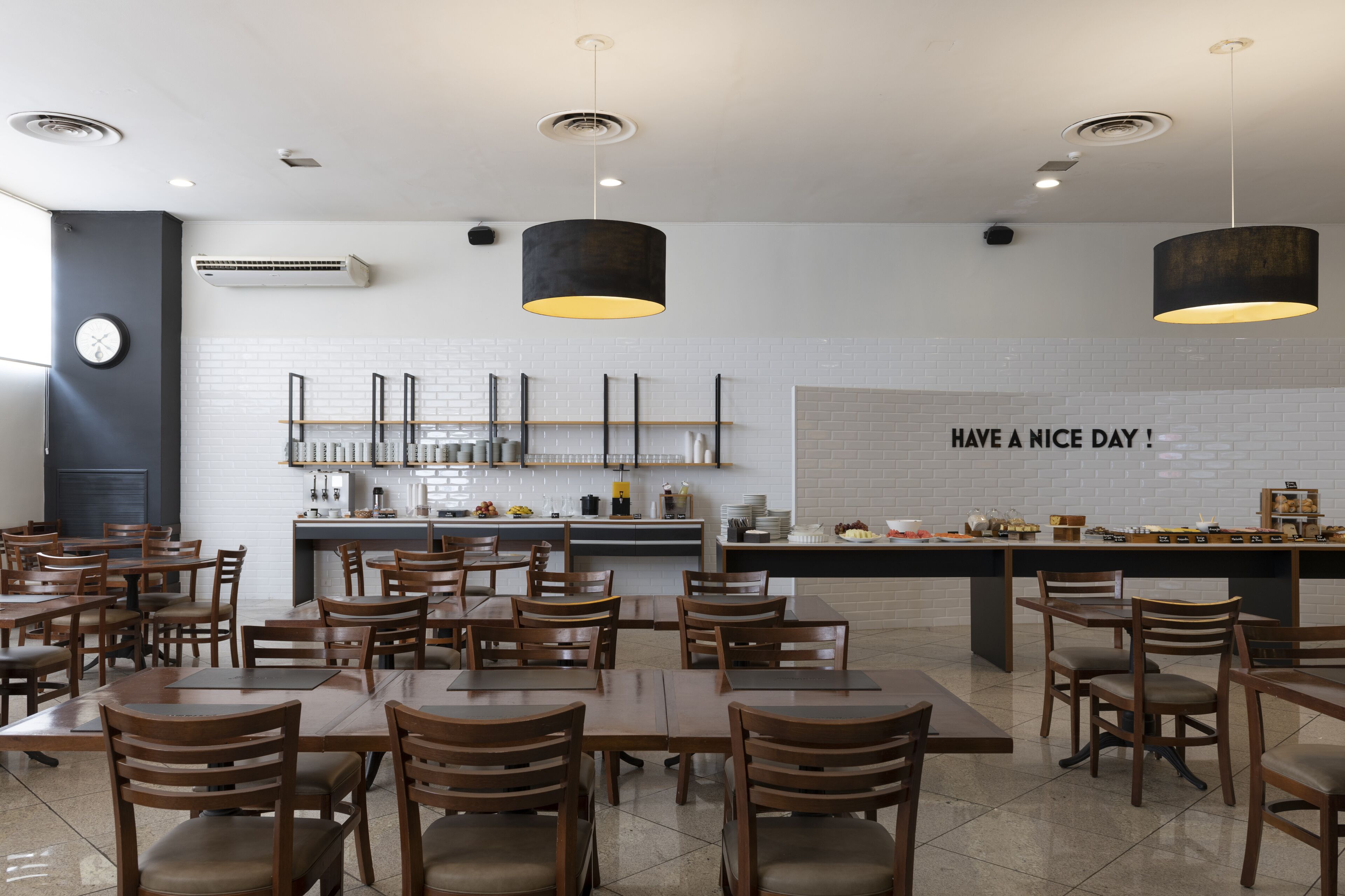 A modern restaurant with wooden tables and chairs, a kitchen area, and a wall with a 'HAVE A NICE DAY!' sign.
