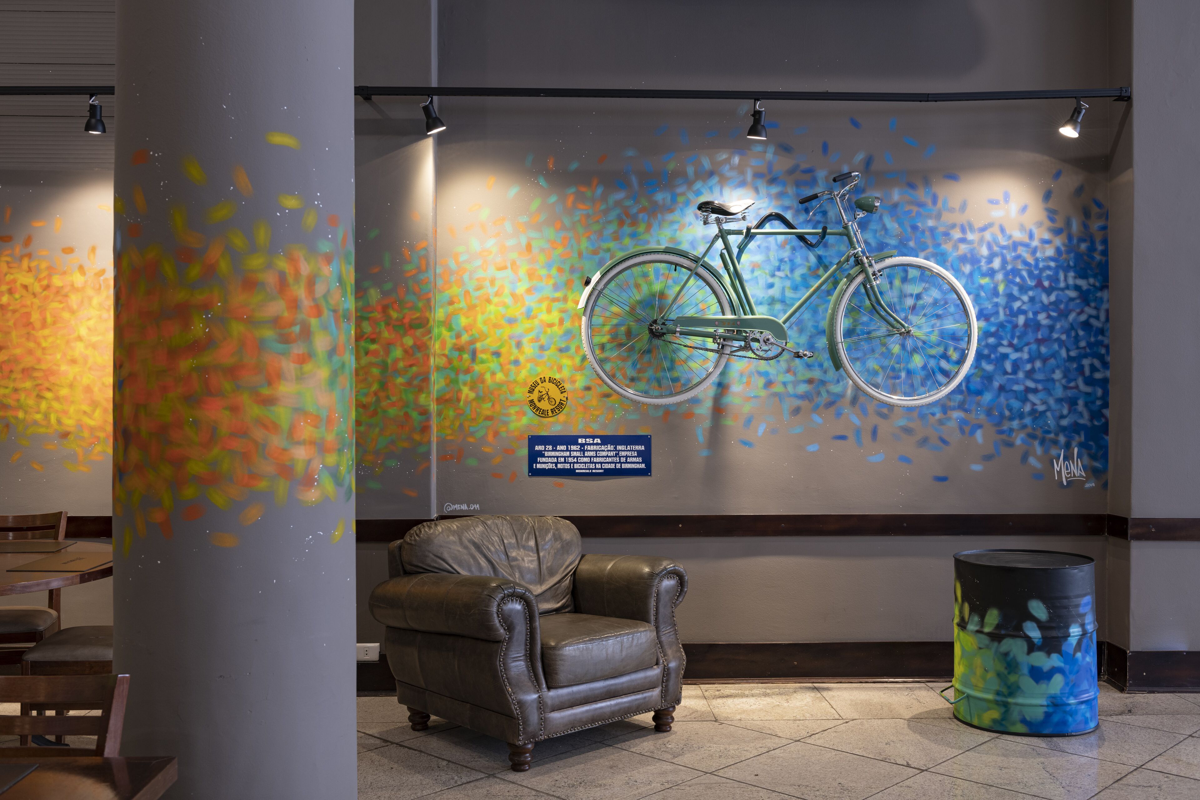 A lobby with a colorful abstract mural, a leather armchair, and a bicycle mounted on the wall.