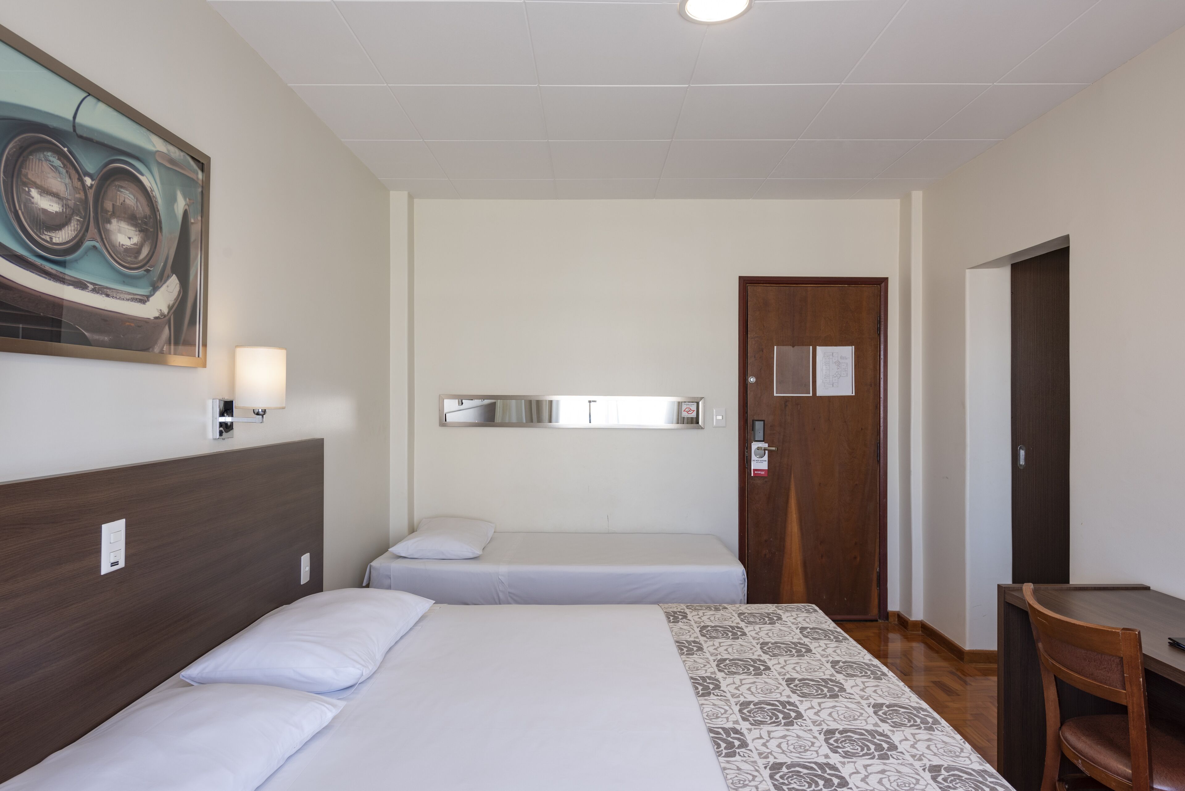 A hotel room with two single beds, a wooden headboard, a desk, and a chair.