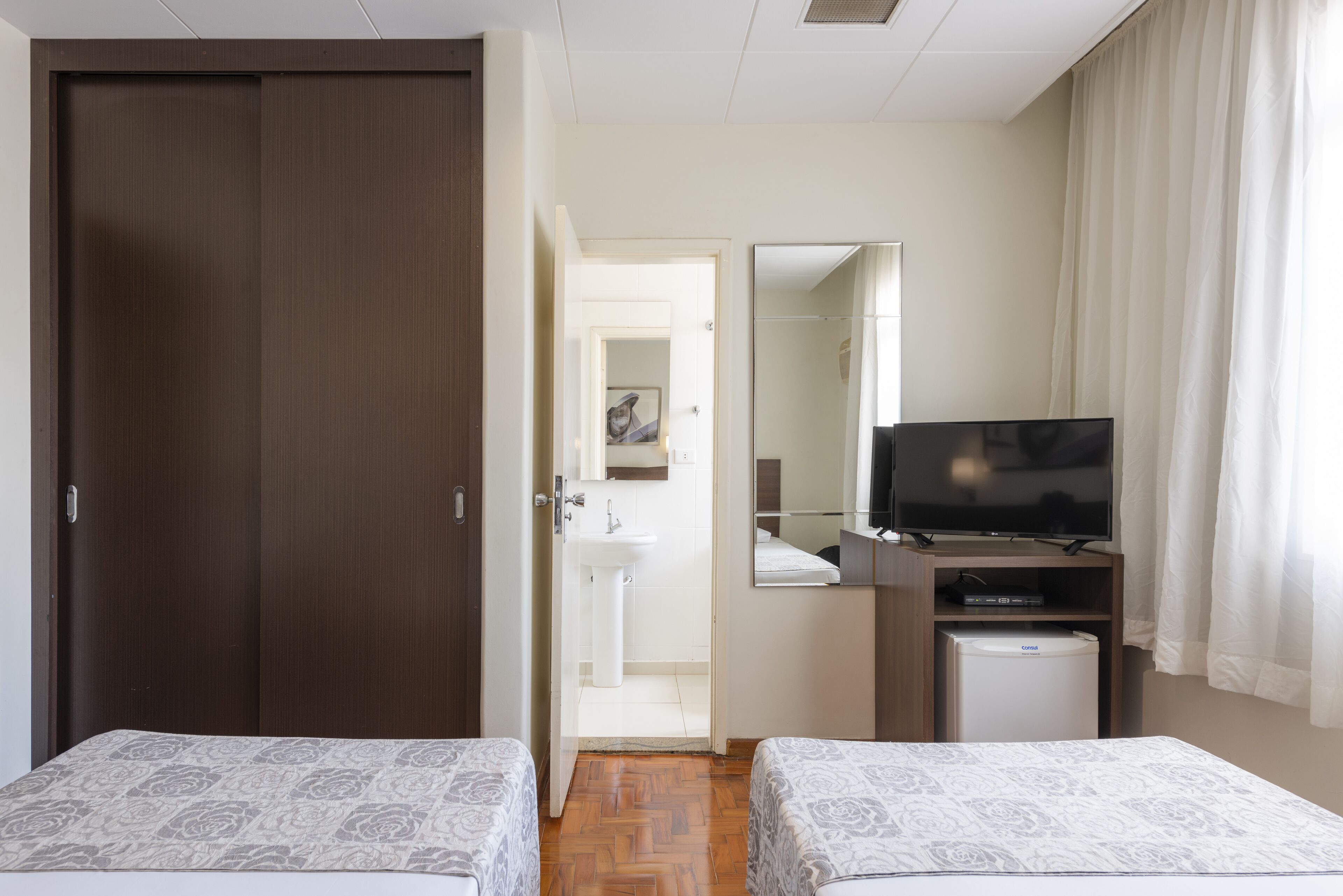 Habitació d'hotel amb dos llits, televisió, nevera petita i un mirall.