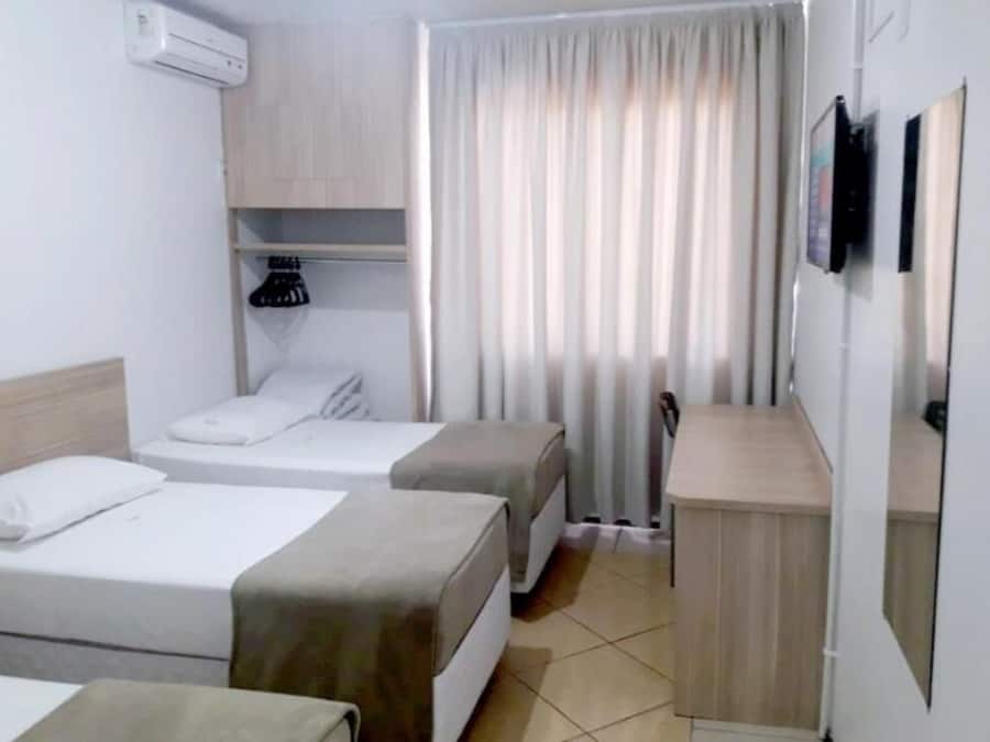 Habitación de hotel con dos camas, un escritorio pequeño, un espejo y una ventana con cortinas.