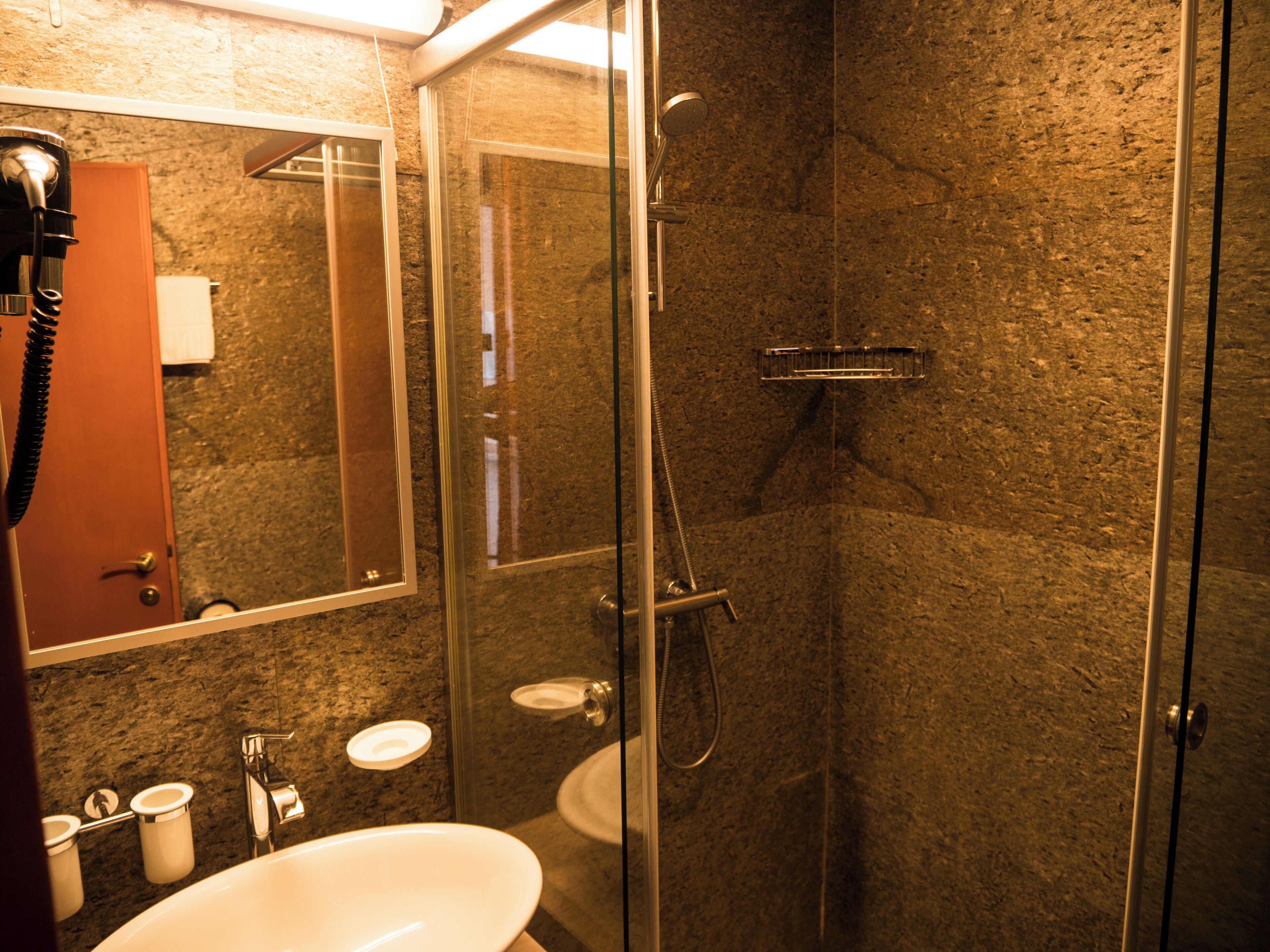 A bathroom with a glass-enclosed shower, a sink, a mirror, and a towel rack.