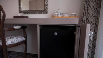 Una kitchenette compacta con refrigerador, una silla, un espejo y una bandeja con utensilios de cocina.