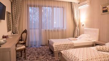 Ein Hotelzimmer mit zwei Betten, einem Schreibtisch, einem Stuhl und einem großen Fenster mit transparenten Vorhängen.