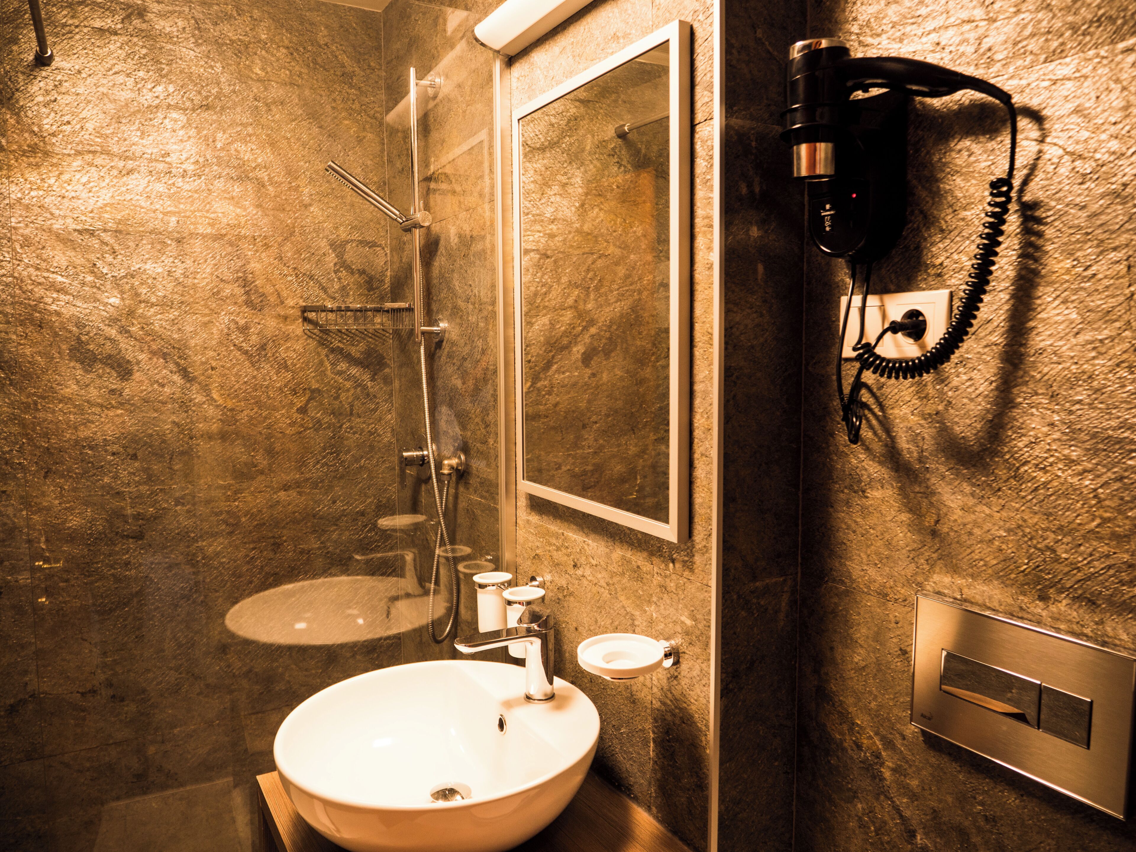 Een badkamer met een wastafel, spiegel, douche en een aan de muur bevestigde telefoon.