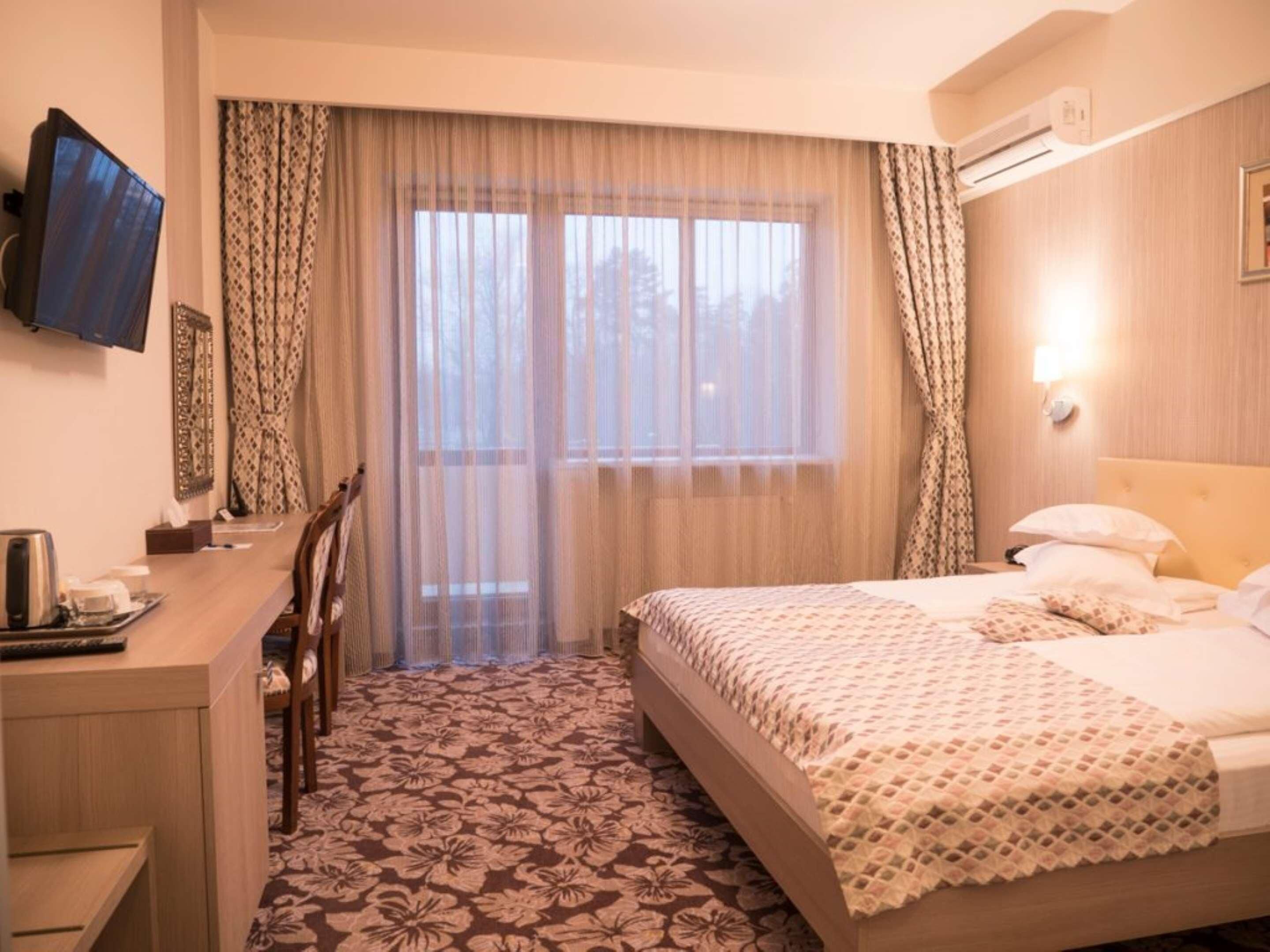 Quarto de hotel com uma cama, uma escrivaninha, uma cadeira e uma televisão na parede.