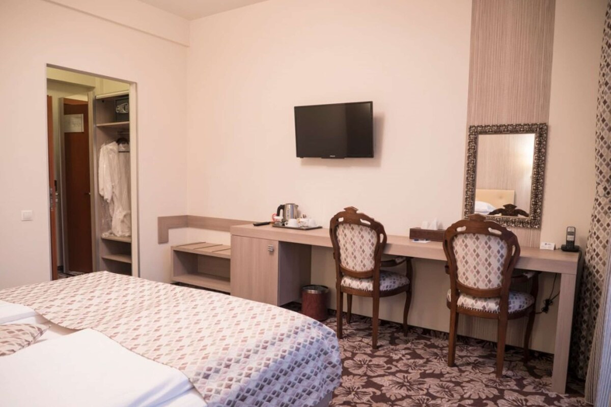Een hotelkamer met een bed, een bureau, twee stoelen, een televisietoestel en een spiegel.
