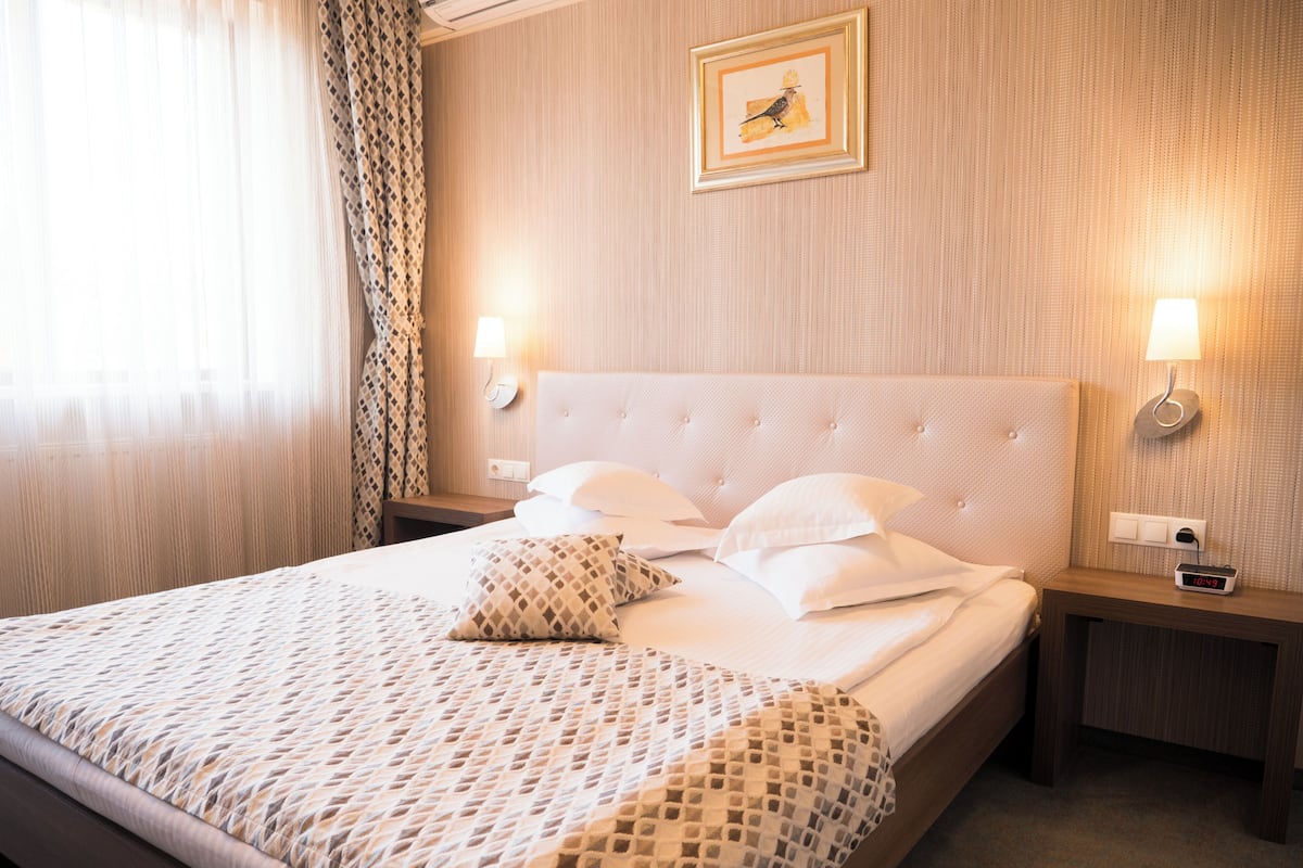 A hotel room with a large bed, two bedside tables, a wall-mounted lamp, and a framed picture.