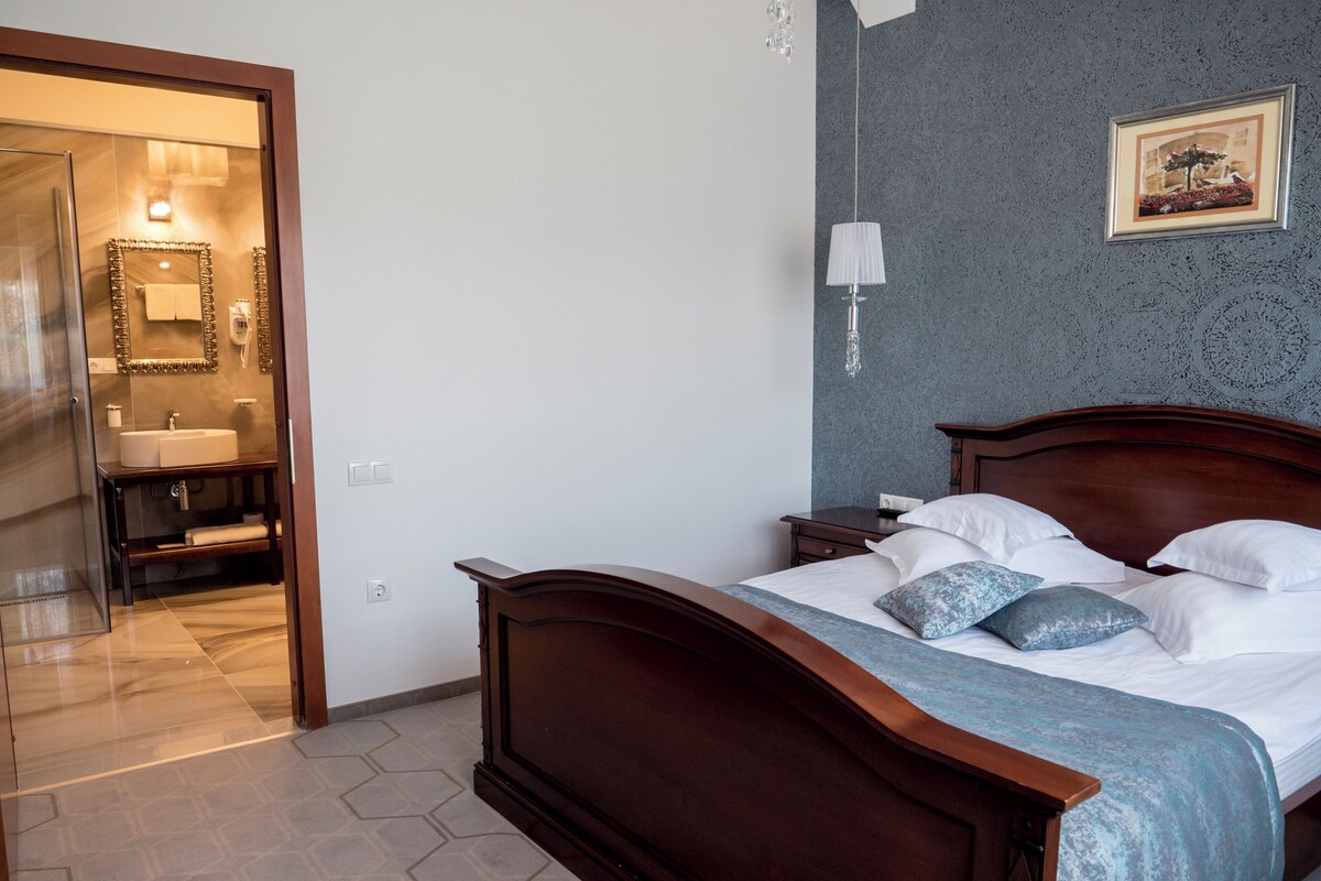 Een slaapkamer met een houten bed, nachtkastje, een wandlamp en een zichtbare badkamer door een open deur.