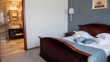 Un dormitorio con una cama de madera, una mesita de noche, una lámpara de pared y un baño visible a través de una puerta abierta.