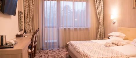 Habitación de hotel con una cama, un escritorio y una silla. Se ve una ventana con cortinas, un equipo de aire acondicionado y un televisor montado en la pared.