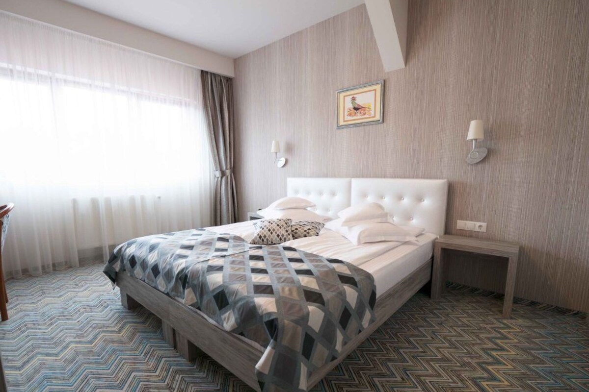 Een hotelkamer met een groot bed, een nachtkastje, een lamp en een schilderij aan de muur.