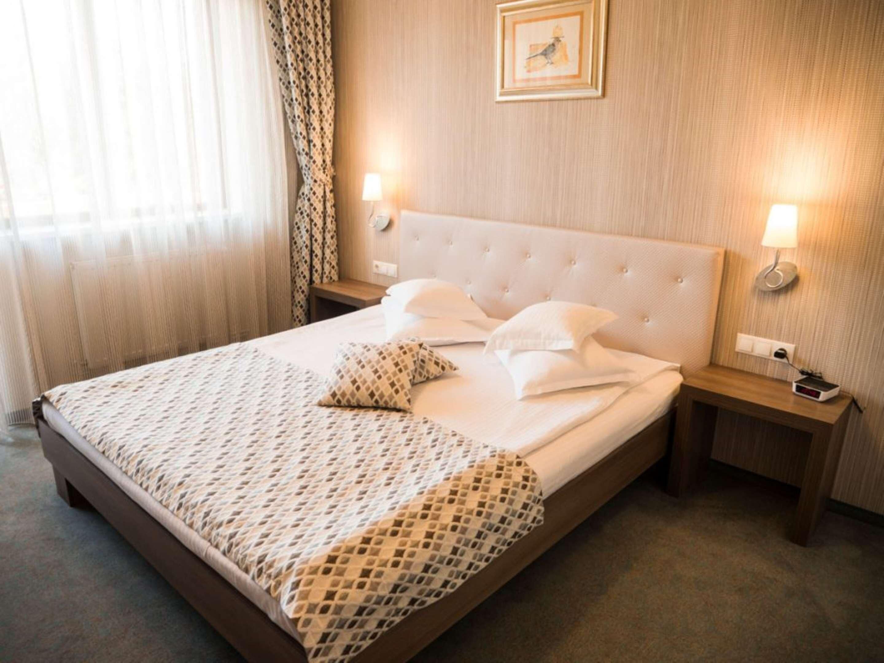 Uma cama bem arrumada com um cobre-leito estampado, duas luminárias de cabeceira e um quadro na parede.