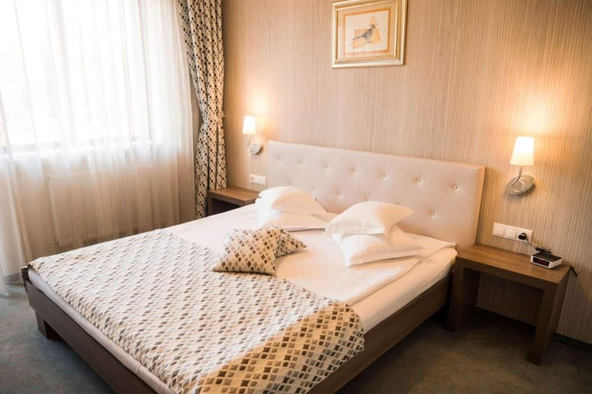 Uma cama bem arrumada com um cobre-leito estampado, duas luminárias de cabeceira e um quadro na parede.