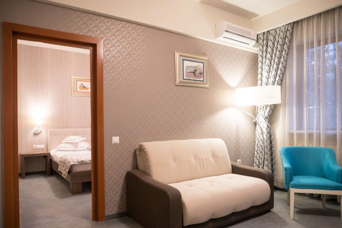Een hotelkamer met een slaapbank, een blauwe fauteuil, een bed en een lamp.
