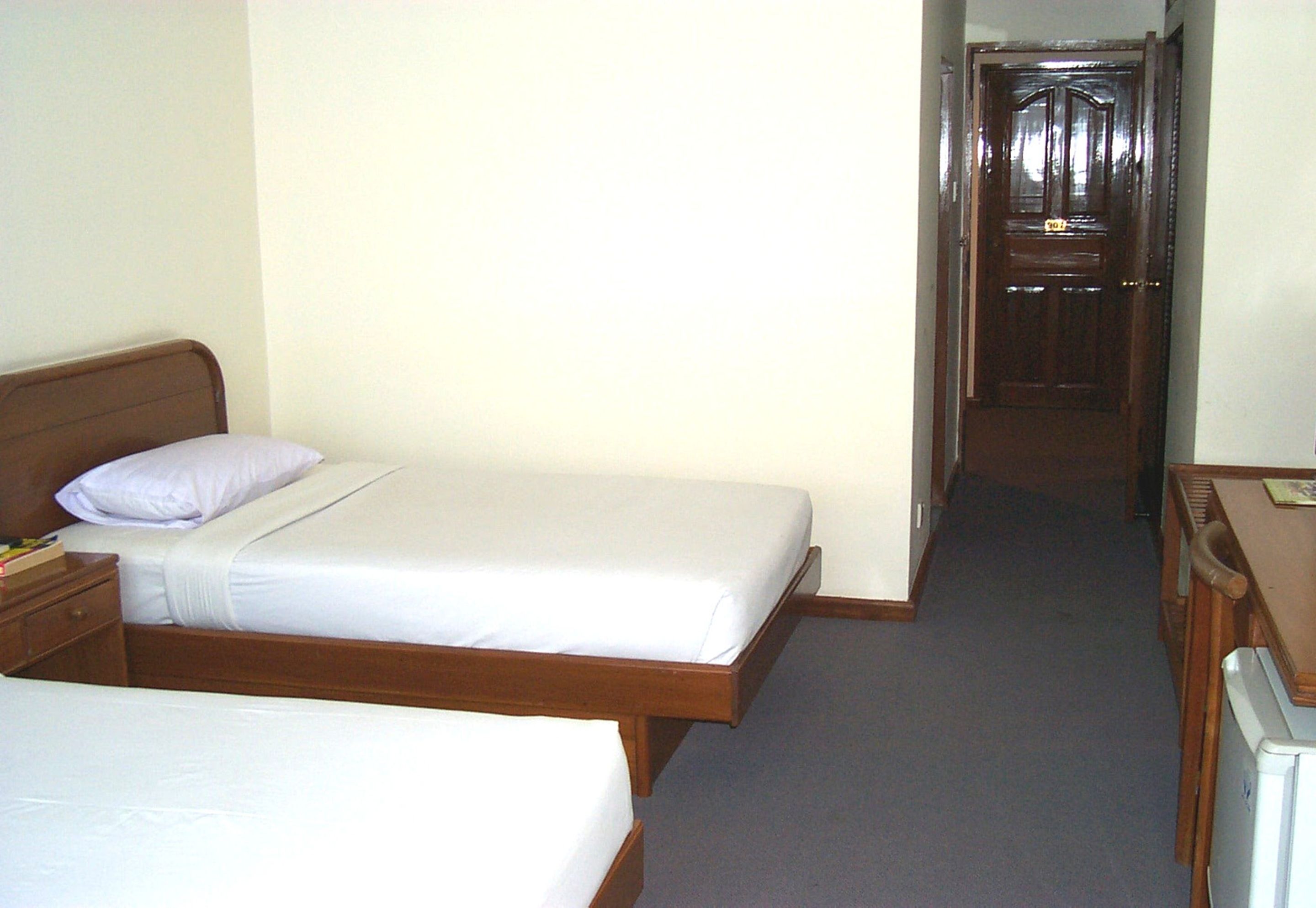 Habitació d'hotel amb un llit individual, una taula de nit, un armari i una porta que dona a una altra habitació.