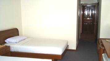 Habitación de hotel con una cama individual, una mesita de noche, un aparador y una puerta que da a otra habitación.