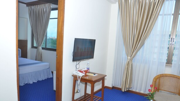 Une chambre d’hôtel avec un lit, une télévision, une table ornée d’un vase de fleurs et une chaise.