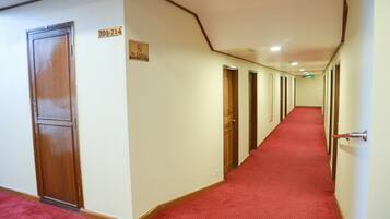 Corredor de hotel com carpete vermelho, portas de madeira e um aviso de 'Não Fumar'.