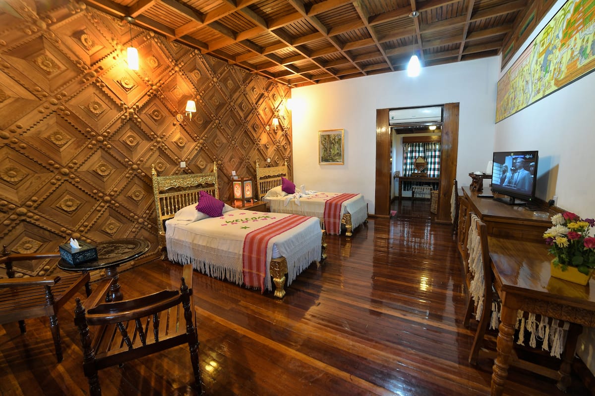 Una habitación con dos camas, muebles de madera, un televisor y un techo decorativo.