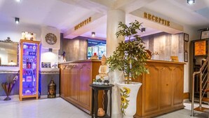 Un área de recepción con un mostrador de madera, una planta en maceta y una estantería con diversos objetos.