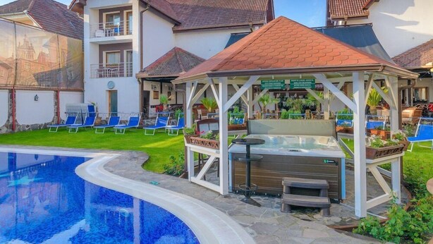 Un área de piscina con sillones reclinables, un jacuzzi y un pabellón.