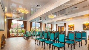 Una habitación amplia con filas de sillas color turquesa y pisos de madera, con ventanas grandes que ofrecen vistas al exterior.