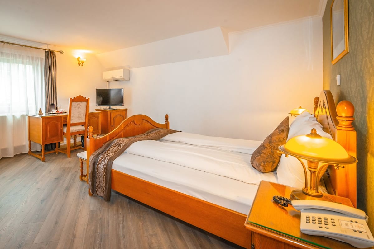 Una habitación de hotel con una cama de madera, un escritorio con televisor, una lámpara y un teléfono.
