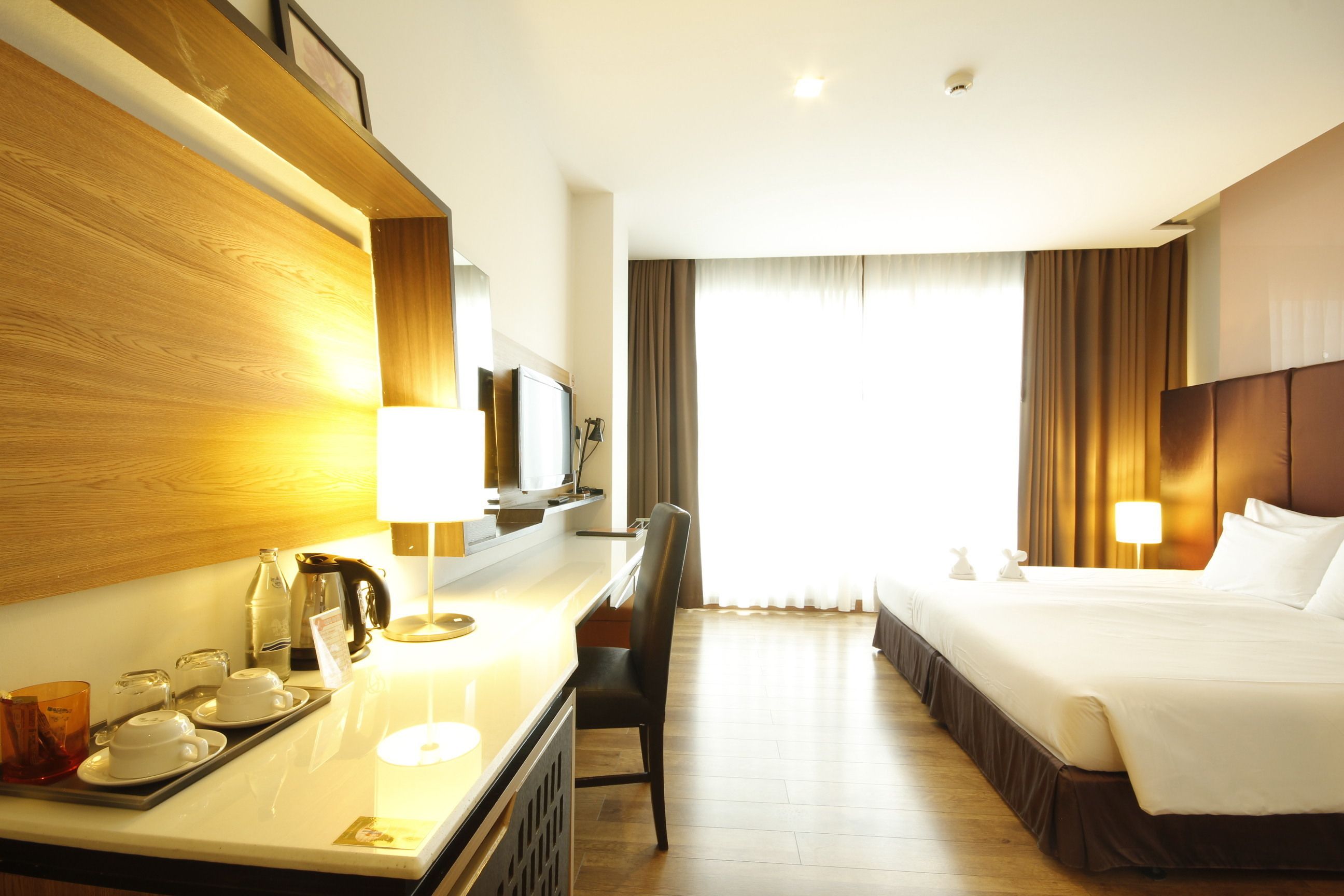 Ein Hotelzimmer mit einem Bett, einem Schreibtisch mit Lampe, einem Sessel und einem Fenster mit Vorhängen.