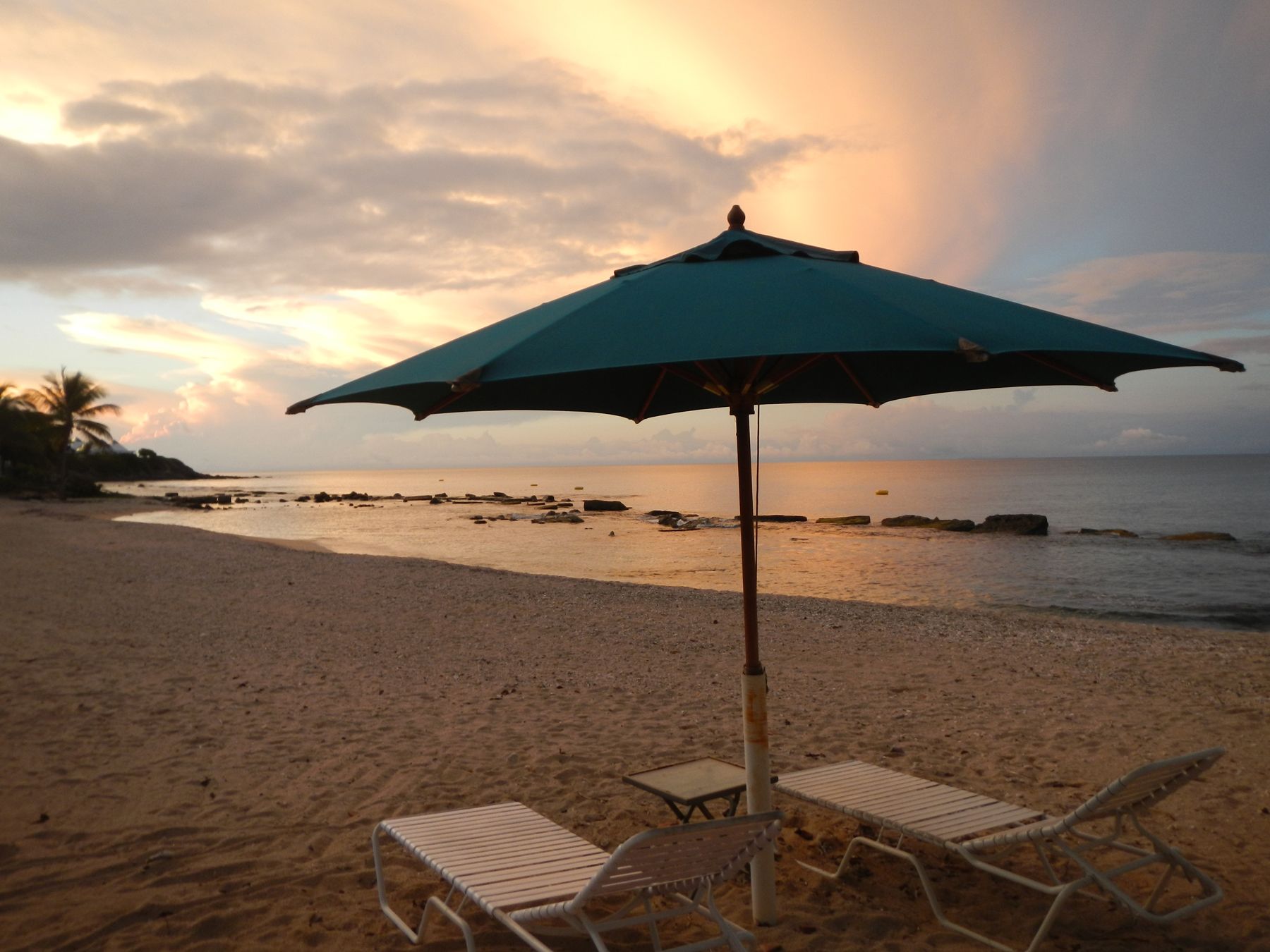 A beach with a single umbrella and two lounge chairs.