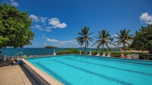 A swimming pool with clear blue water, surrounded by palm trees and a view of the ocean.