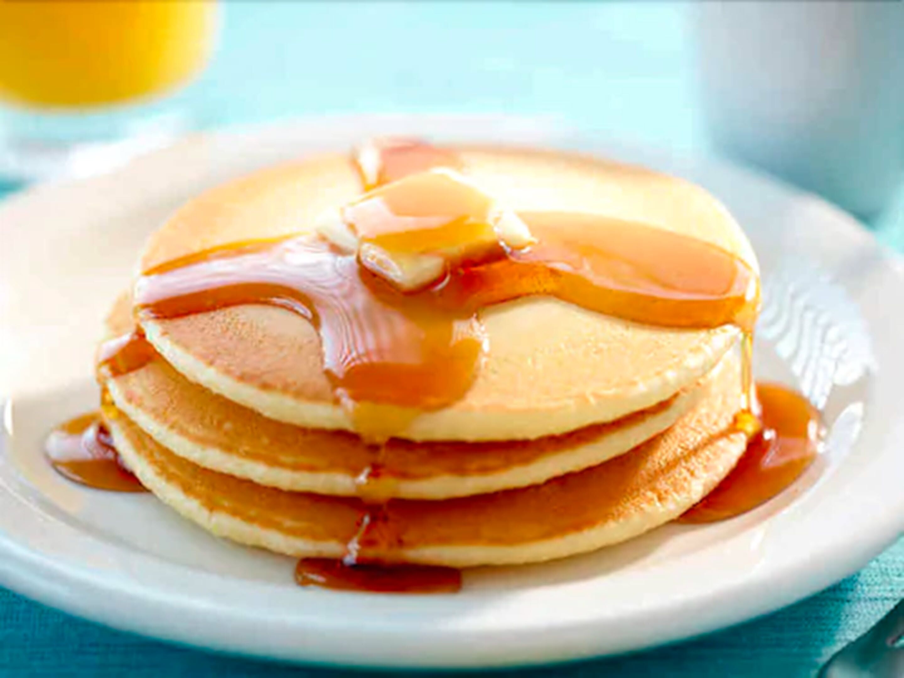 Une pile de crêpes arrosées de sirop, servies dans une assiette blanche.