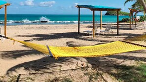 A beach with a hammock, palm trees, and a clear blue sky.