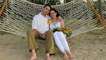 A couple sitting in a hammock on a sandy beach.