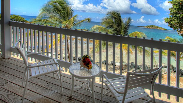 A wooden deck with white metal chairs and a small table with a flower vase.