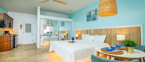A hotel room with a bed, a dining table with plates, a ceiling fan, and a wall-mounted lamp.