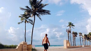 A man walking on a paved pathway with palm trees and a beach in the background. - Beach and Town Motel (Hollywood)