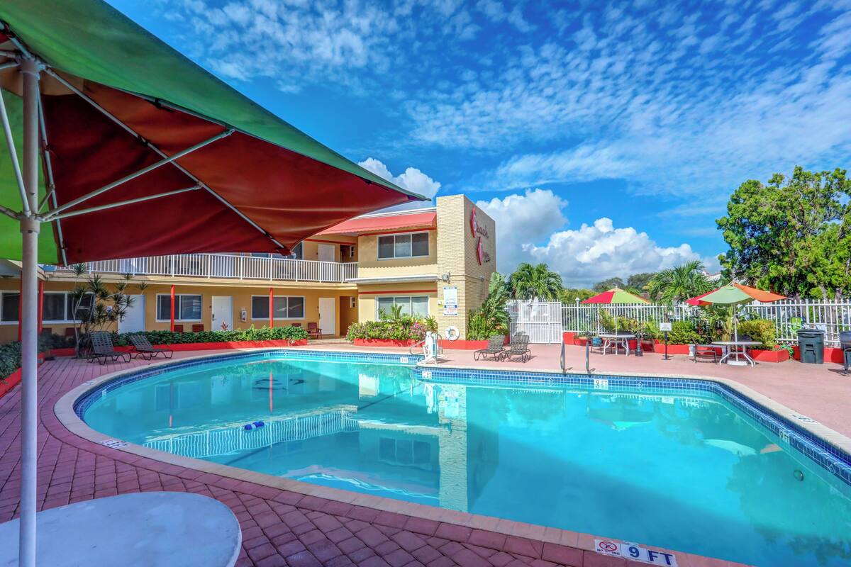 A swimming pool with a red canopy, a building with a red roof, and a fenced area with outdoor seating.
