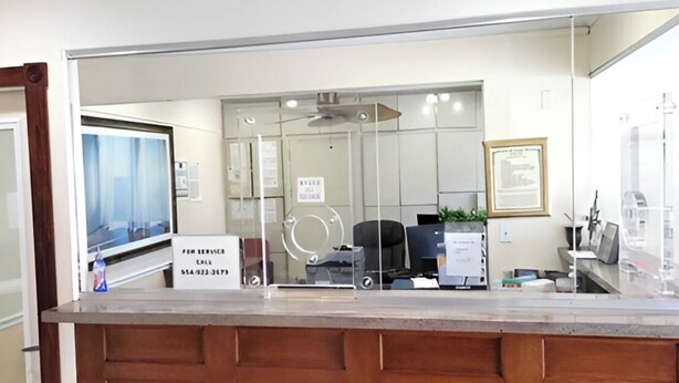 A reception desk with a glass partition, a computer, and a framed picture on the wall. - Beach and Town Motel (Hollywood)