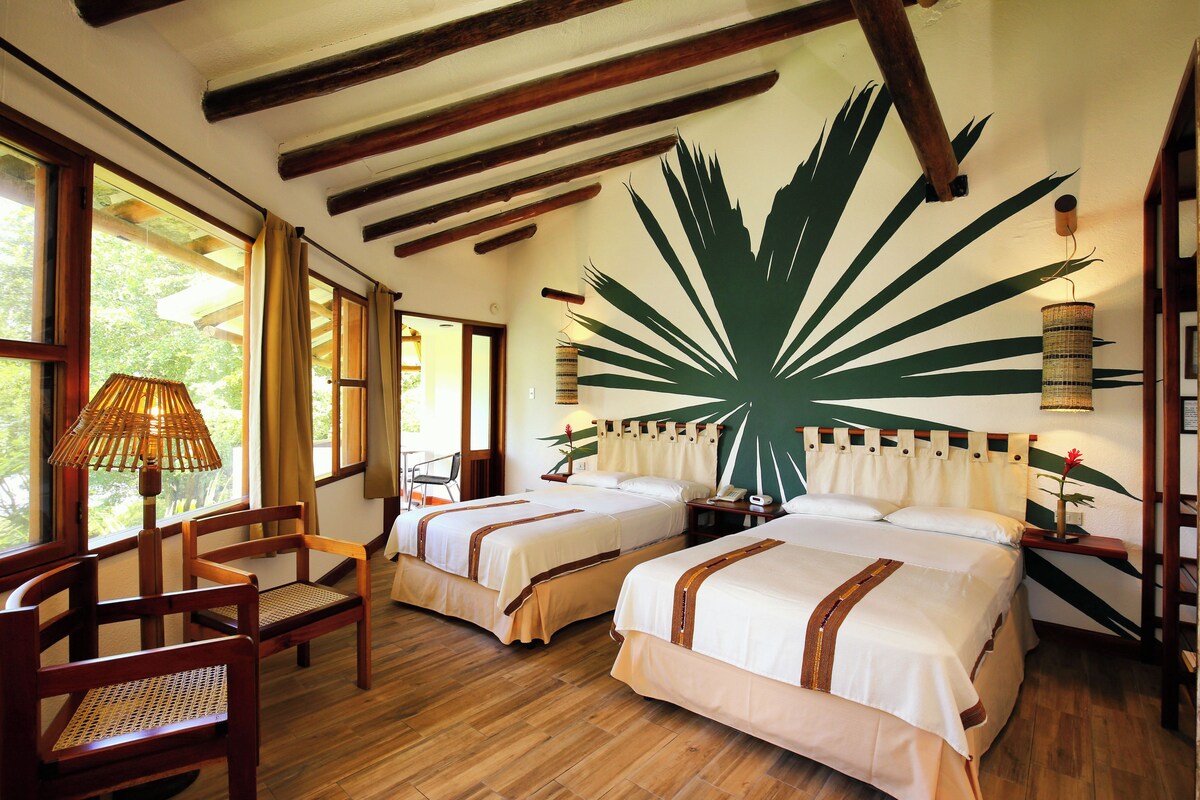 Una habitación con dos camas, piso de madera y un gran mural con hojas tropicales.