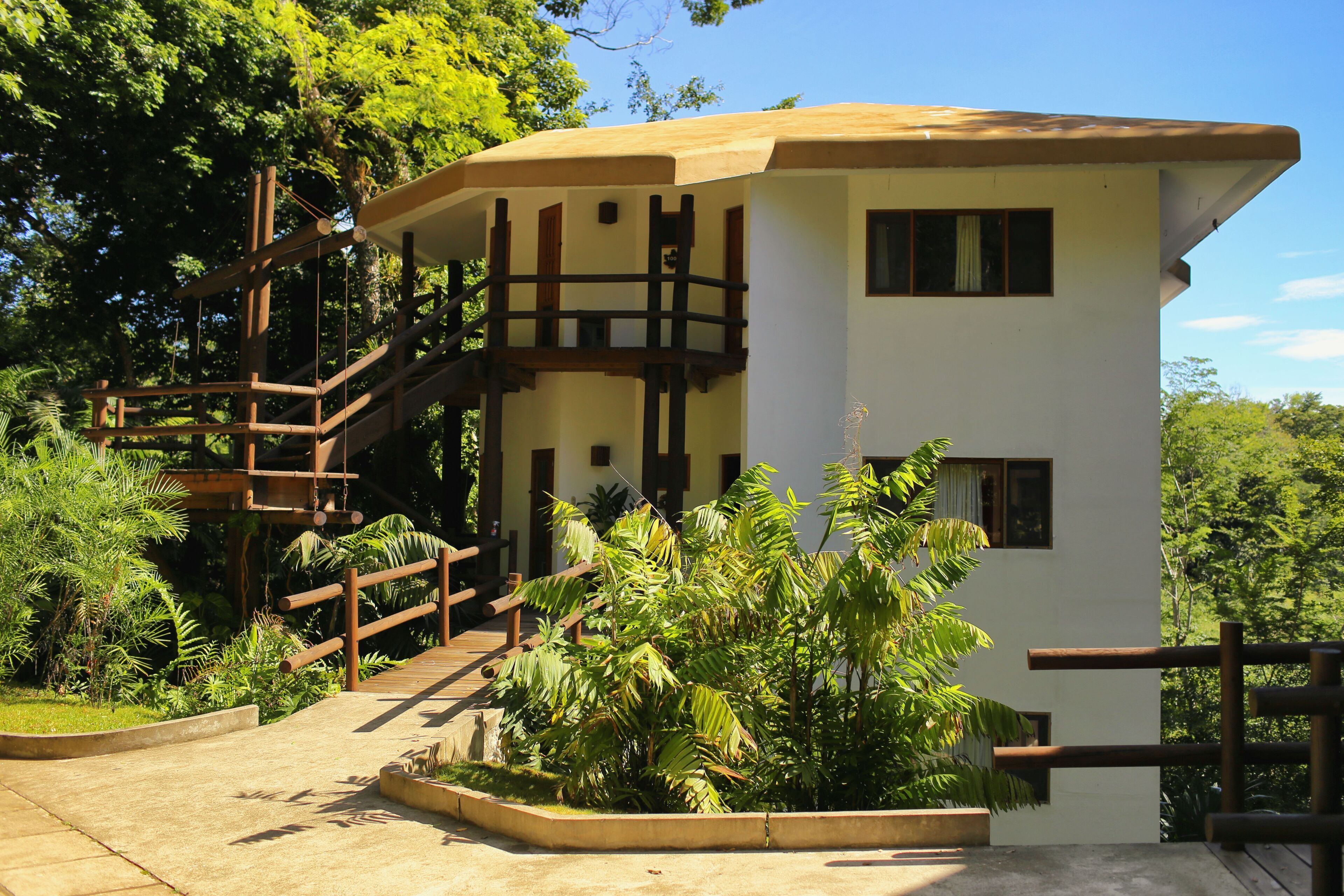 Un edificio su due piani con una scala in legno e un balcone, immerso nel verde.