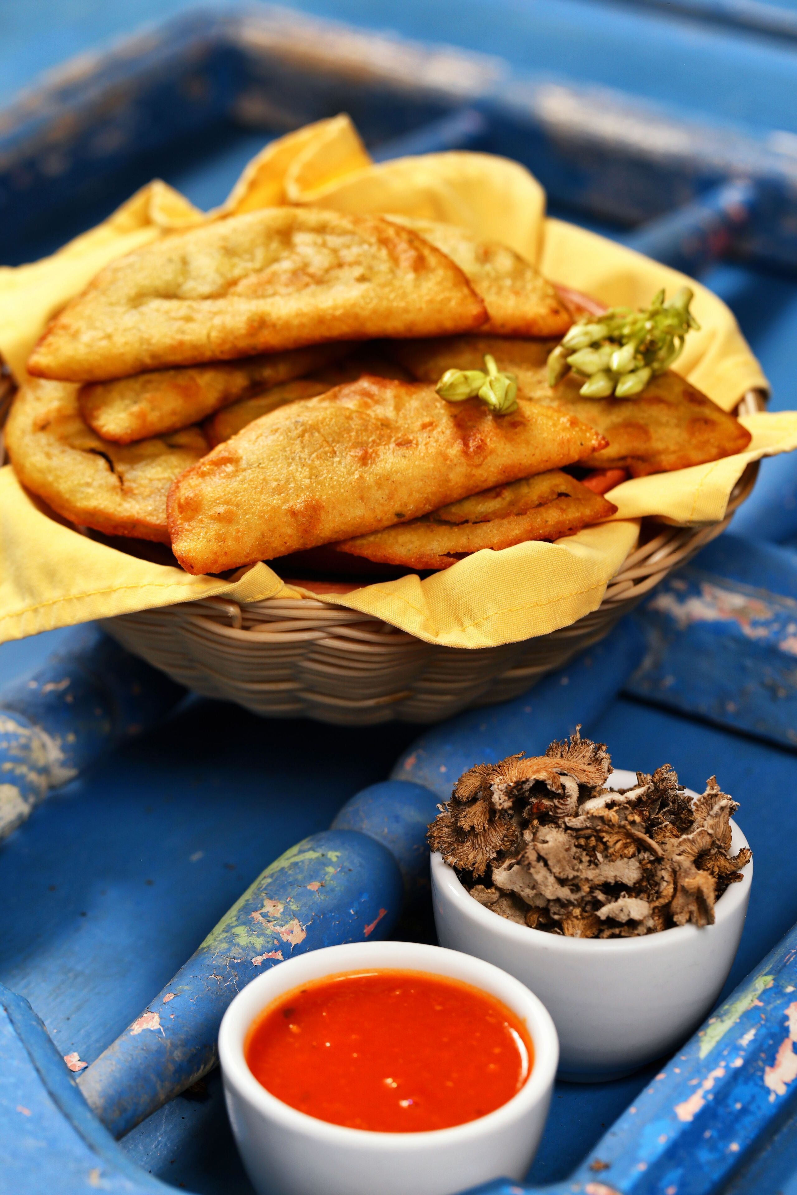 Un panier de pâtisseries frites, accompagné d’une sauce rouge et d’un bol de champignons séchés.