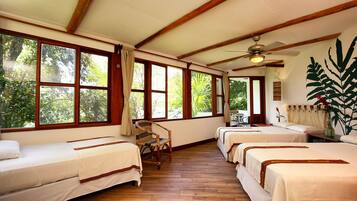 Habitación con tres camas, pisos de madera, ventanas amplias y un ventilador de techo.