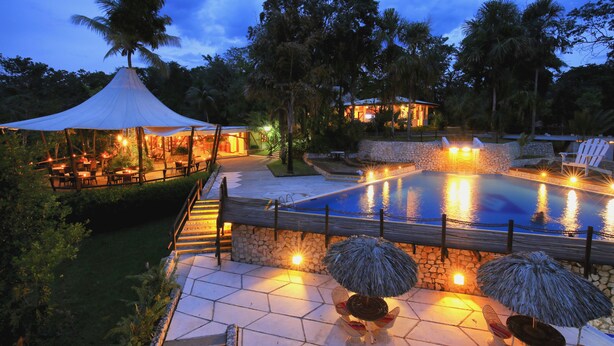 A pool area with a stone wall, lounge chairs, and umbrellas. - Hotel Villa Maya (Flores)