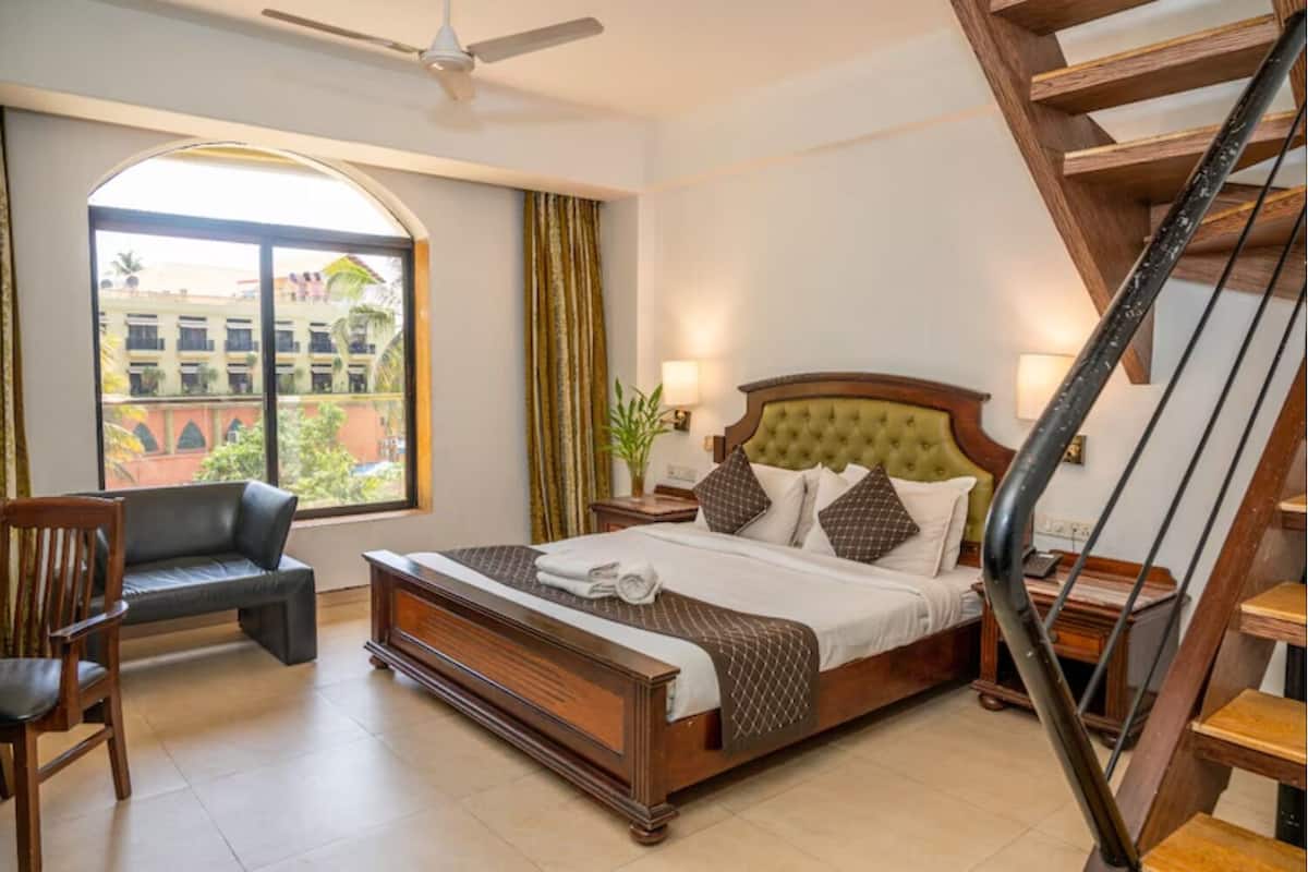 Un dormitorio con cama, una silla, una escalera y vistas de edificios.