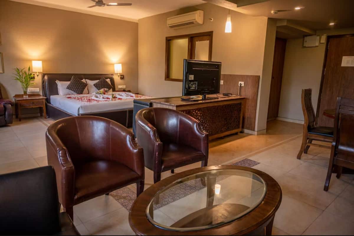 Una habitación de hotel con cama, escritorio, televisor, sillones de cuero y una mesa de centro de vidrio.