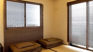 A tatami mat room with a low ceiling, wooden beams, a window with a view, and a sliding door. - Kyoto Guesthouse Roujiya (Kyoto)