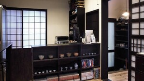 A room with a wooden floor, a bookshelf, a kitchen area, and a sliding door. - Kyoto Guesthouse Roujiya (Kyoto)